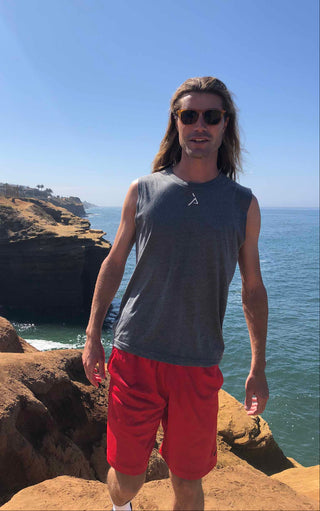 Man standing on a rocky cliff overlooking the ocean with sunglasses on